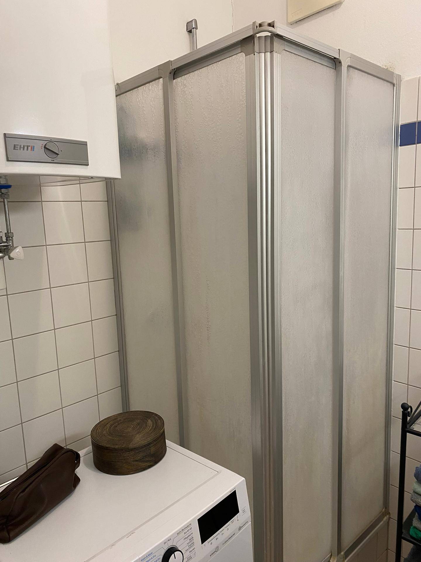 Badezimmer mit Duschkabine, Waschmaschine und weißen Wandfliesen.