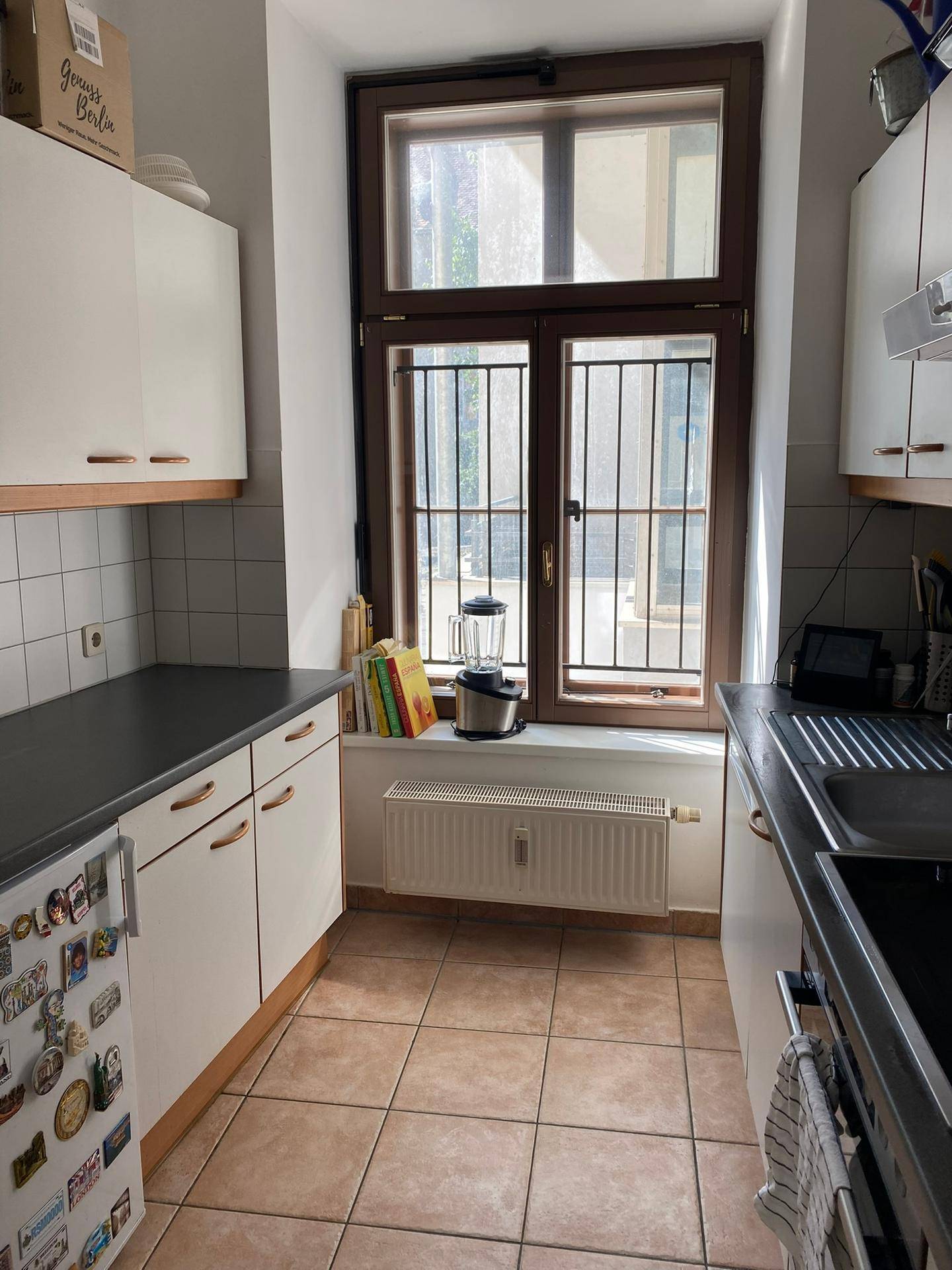 Helle Küche mit weißen Schränken, Fenster und Fliesenboden.