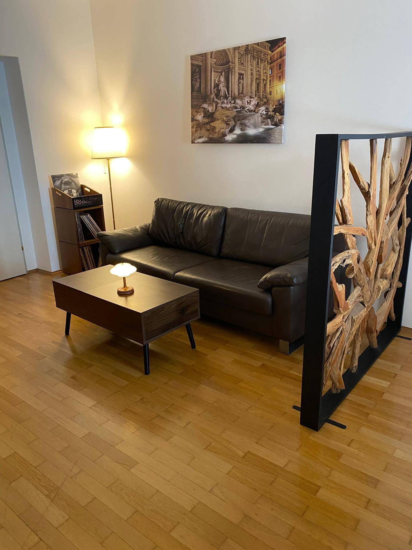 Gemütlicher Wohnbereich mit dunklem Ledersofa, Couchtisch und Stehlampe.
