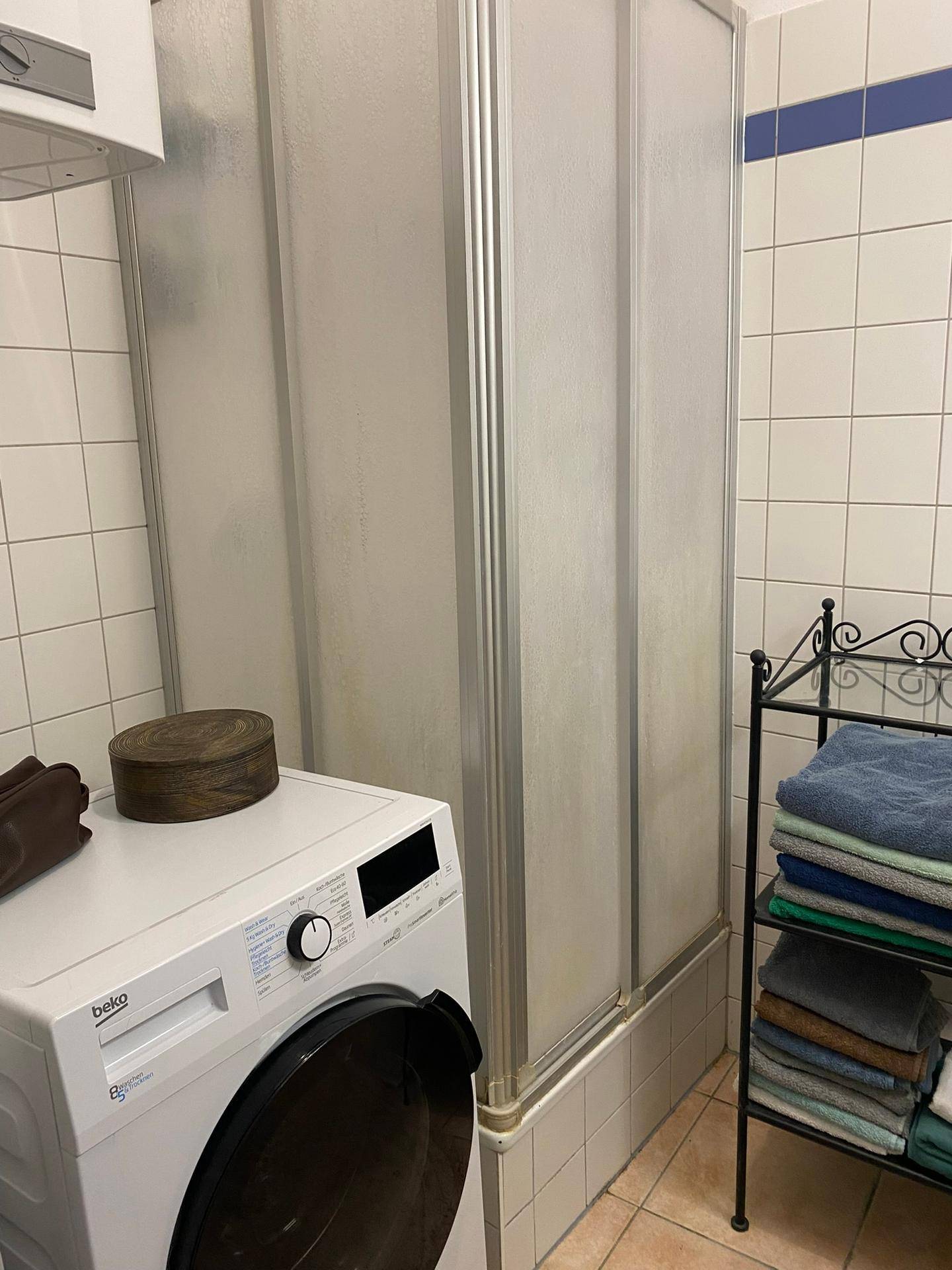 Funktionales Badezimmer mit Duschkabine, Waschmaschine und Handtuchregal.
