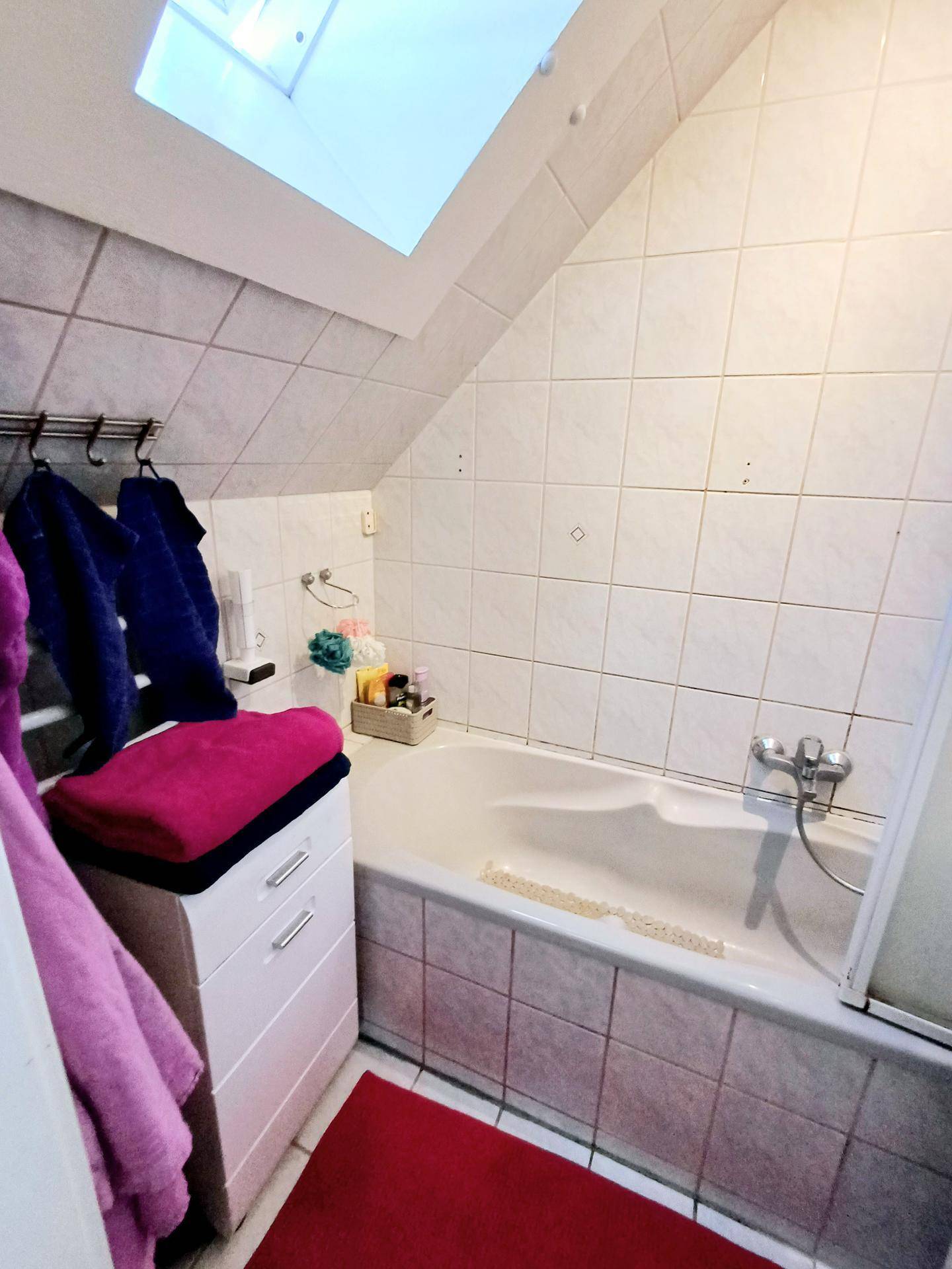 Badezimmer mit Badewanne, Fliesenwänden und einem Dachfenster für natürliches Licht.
