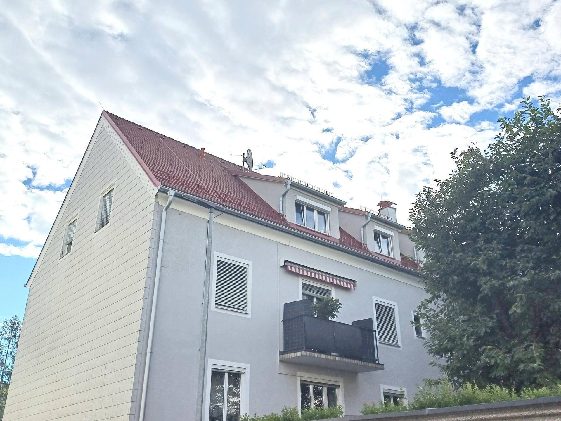 Mehrfamilienhaus mit Mansarddach, Balkon und Rollläden unter bewölktem Himmel.