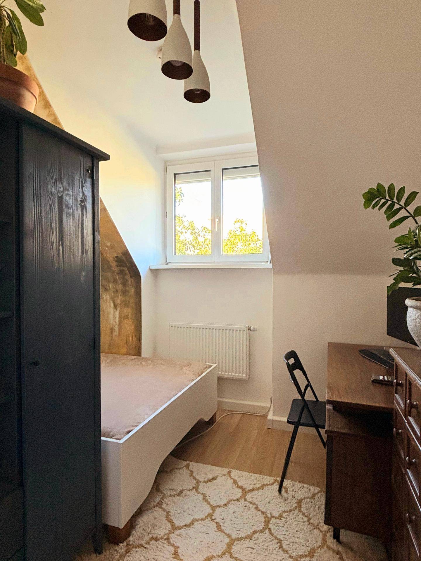 Gemütliches Schlafzimmer mit Einzelbett, Holzmöbeln und Teppich, unter einer Dachschräge.