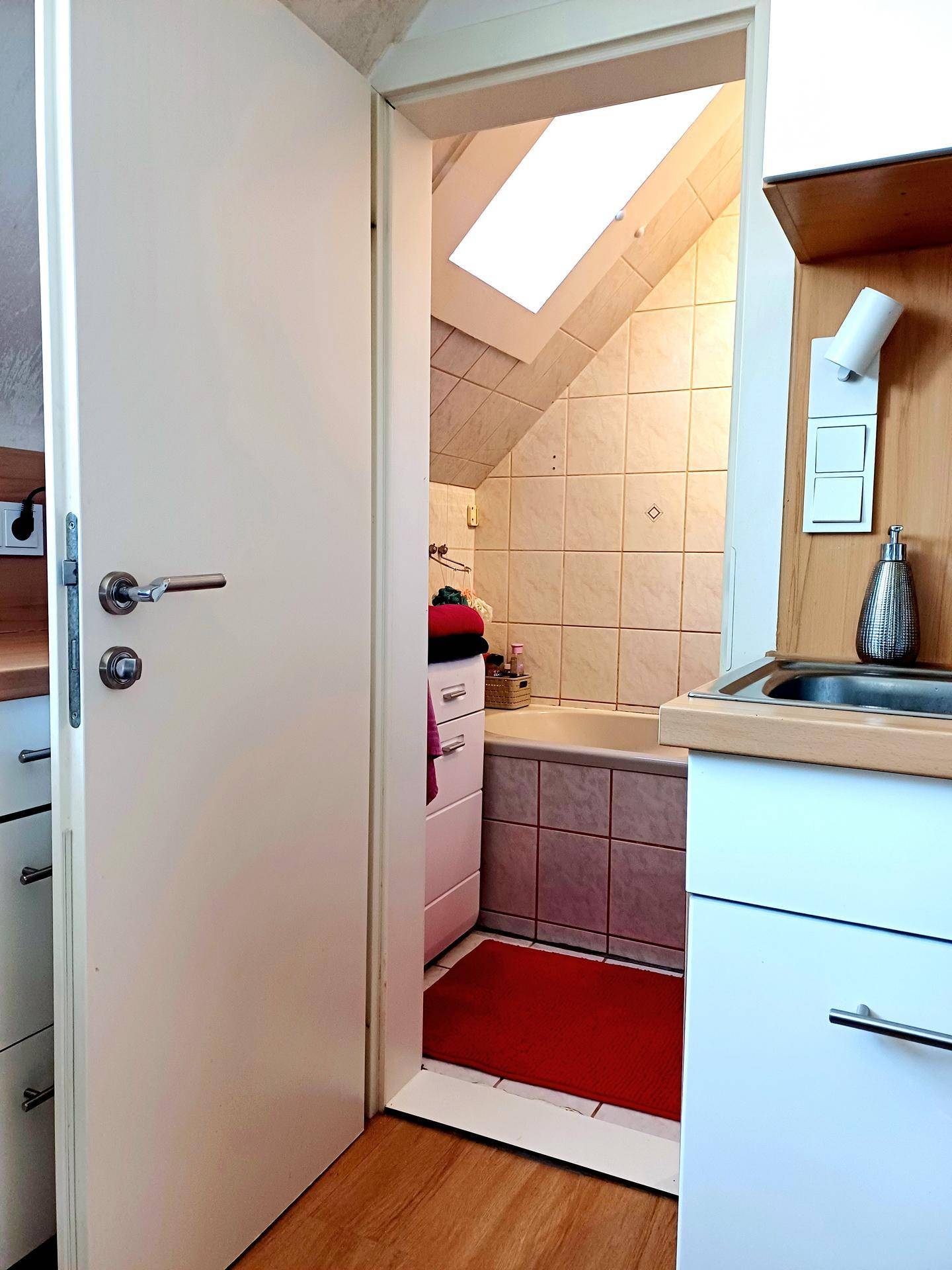 Eingang zum Badezimmer mit kleiner Waschecke und Blick auf die Badewanne unter dem Dachfenster.