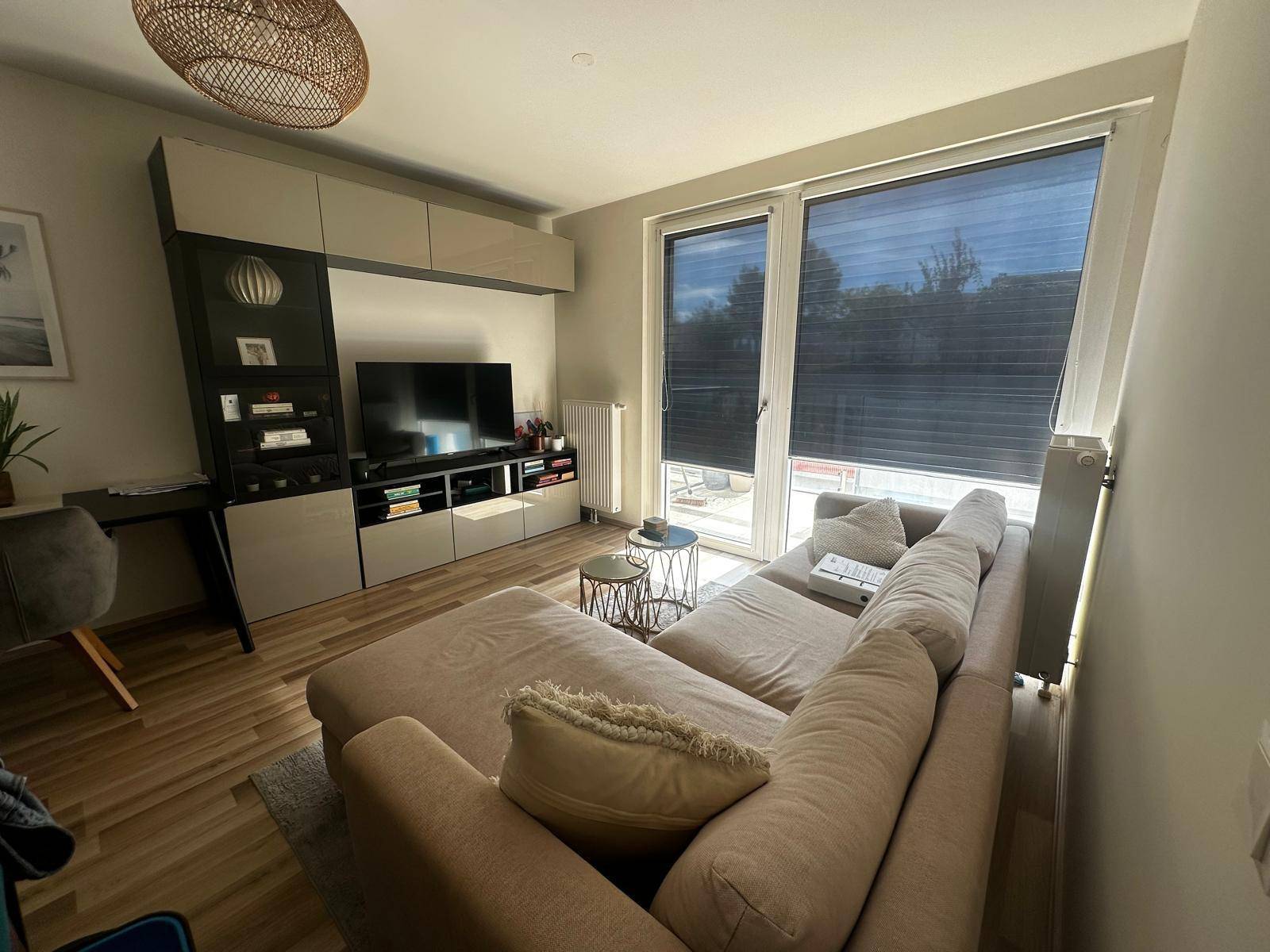 Heller Wohnbereich mit beigem Ecksofa, TV-Möbel und Zugang zu einem Außenbereich.