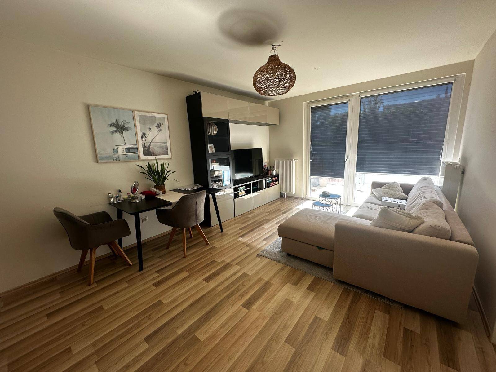 Gemütliches Wohnzimmer mit Sofa, Esstisch und großen Fenstern, die viel Licht hereinlassen.