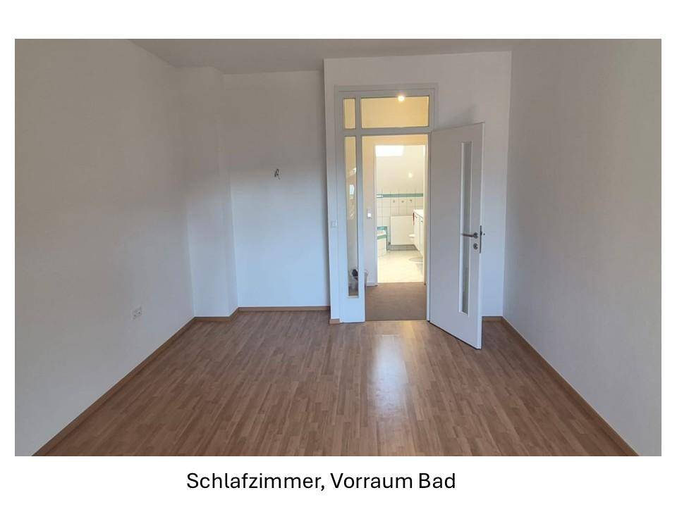 Leeres Schlafzimmer mit Holzboden und Zugang zu einem Vorraum oder Badezimmer.