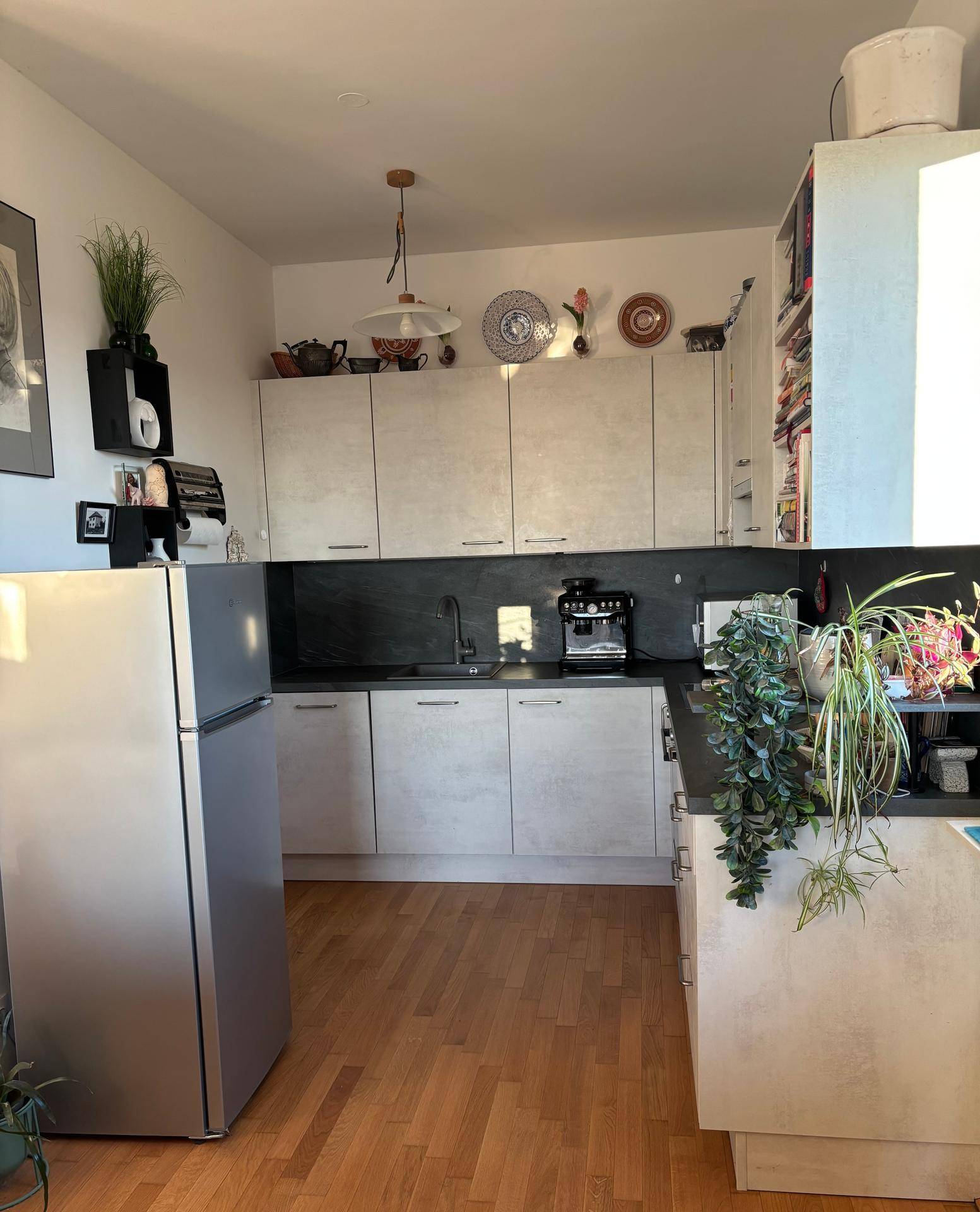 Helle Küche mit grauen Schränken, dunkler Arbeitsplatte und Holzfußboden, ausgestattet mit einem Kühlschrank.