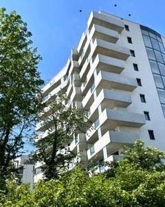 Moderne Wohngebäude-Fassade mit zahlreichen Balkonen und großen Glasflächen unter blauem Himmel.