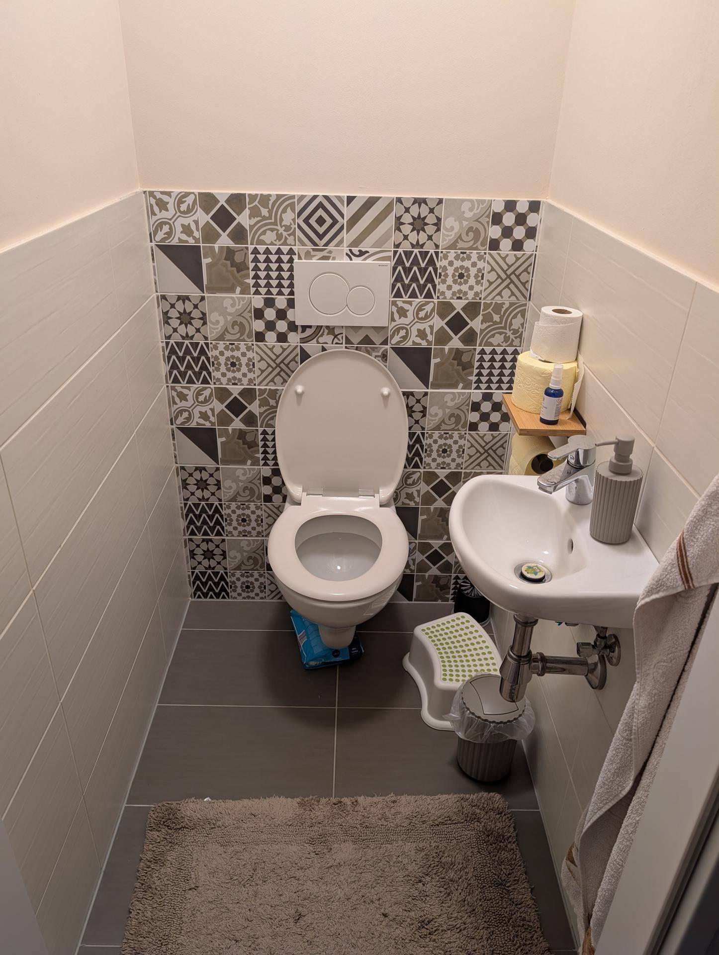 Separates Gäste-WC mit modern gefliesten Wänden und kleinem Handwaschbecken.