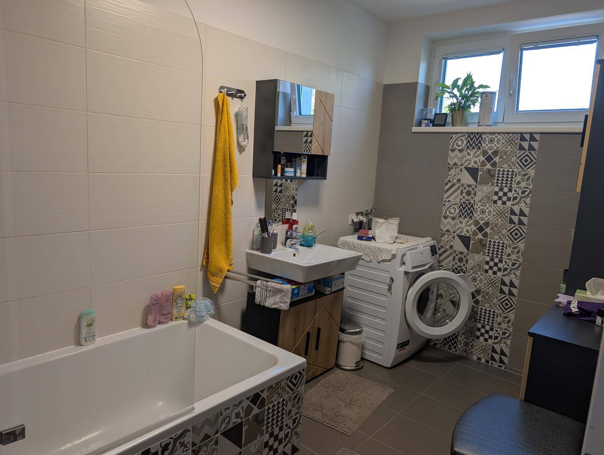 Badezimmer mit Badewanne, Waschbecken, Waschmaschine und einem Fenster für Tageslicht.