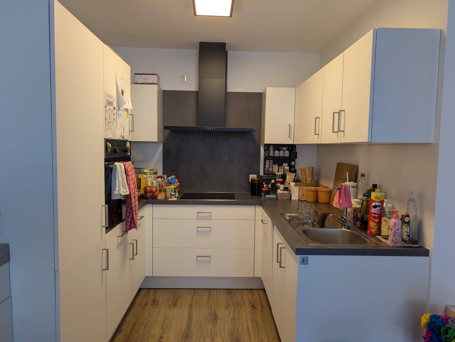 Funktionale Küche mit weißen Schränken, integriertem Backofen und Dunstabzugshaube.