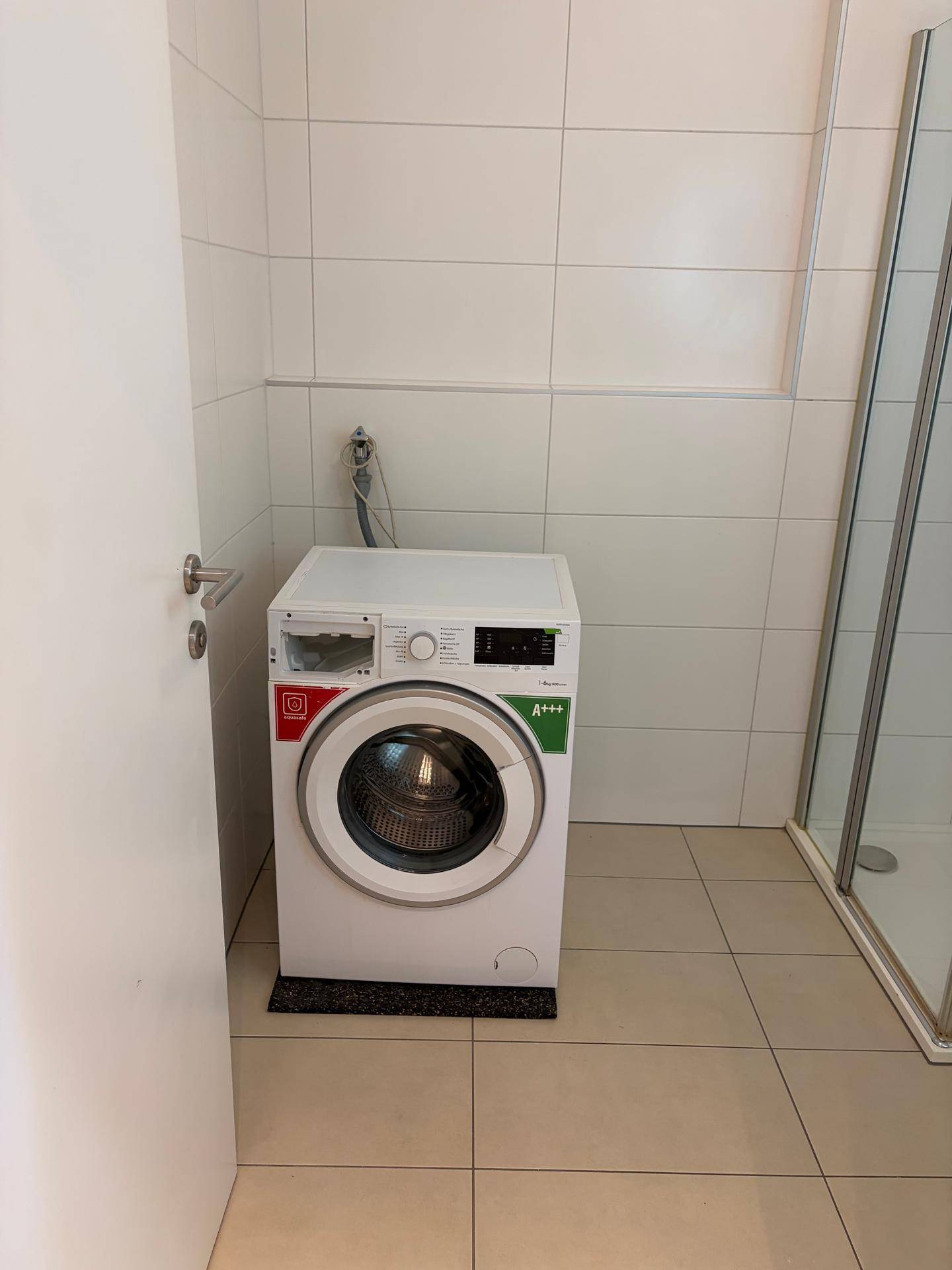 Waschküche mit Waschmaschine und Duschkabine, komplett gefliest.