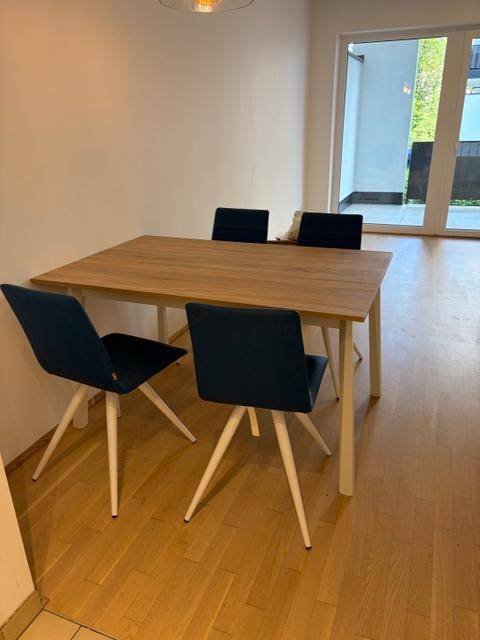 Essbereich mit Holztisch und blauen Stühlen, heller Raum mit Balkonzugang.