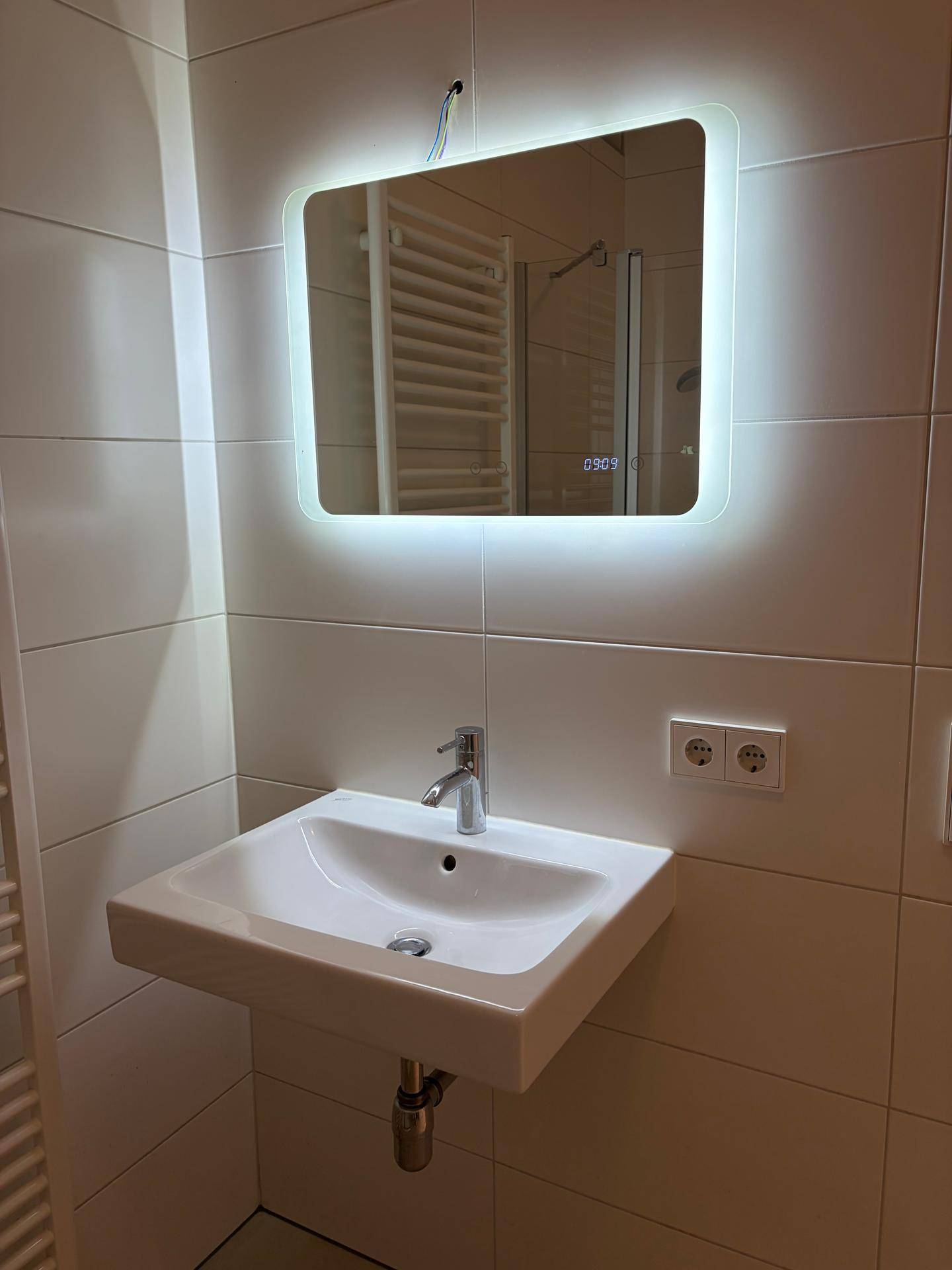 Modernes Badezimmer mit Waschbecken und beleuchtetem Spiegel, hell gefliest.