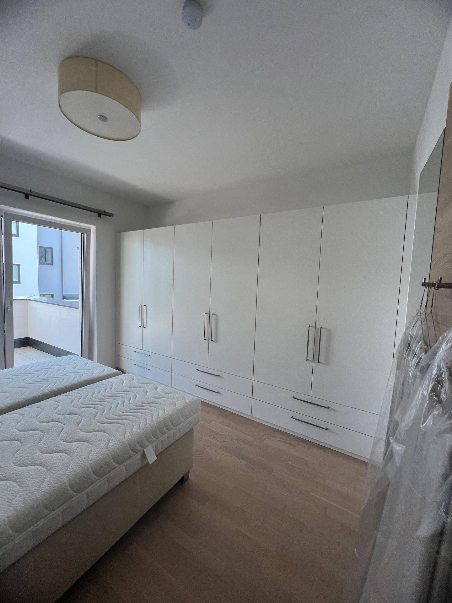 Schlafzimmer mit Doppelbett und großem, weißem Einbauschrank, heller Holzboden.