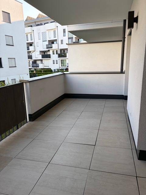 Geräumiger Balkon mit Fliesenboden und Blick auf moderne Wohngebäude.