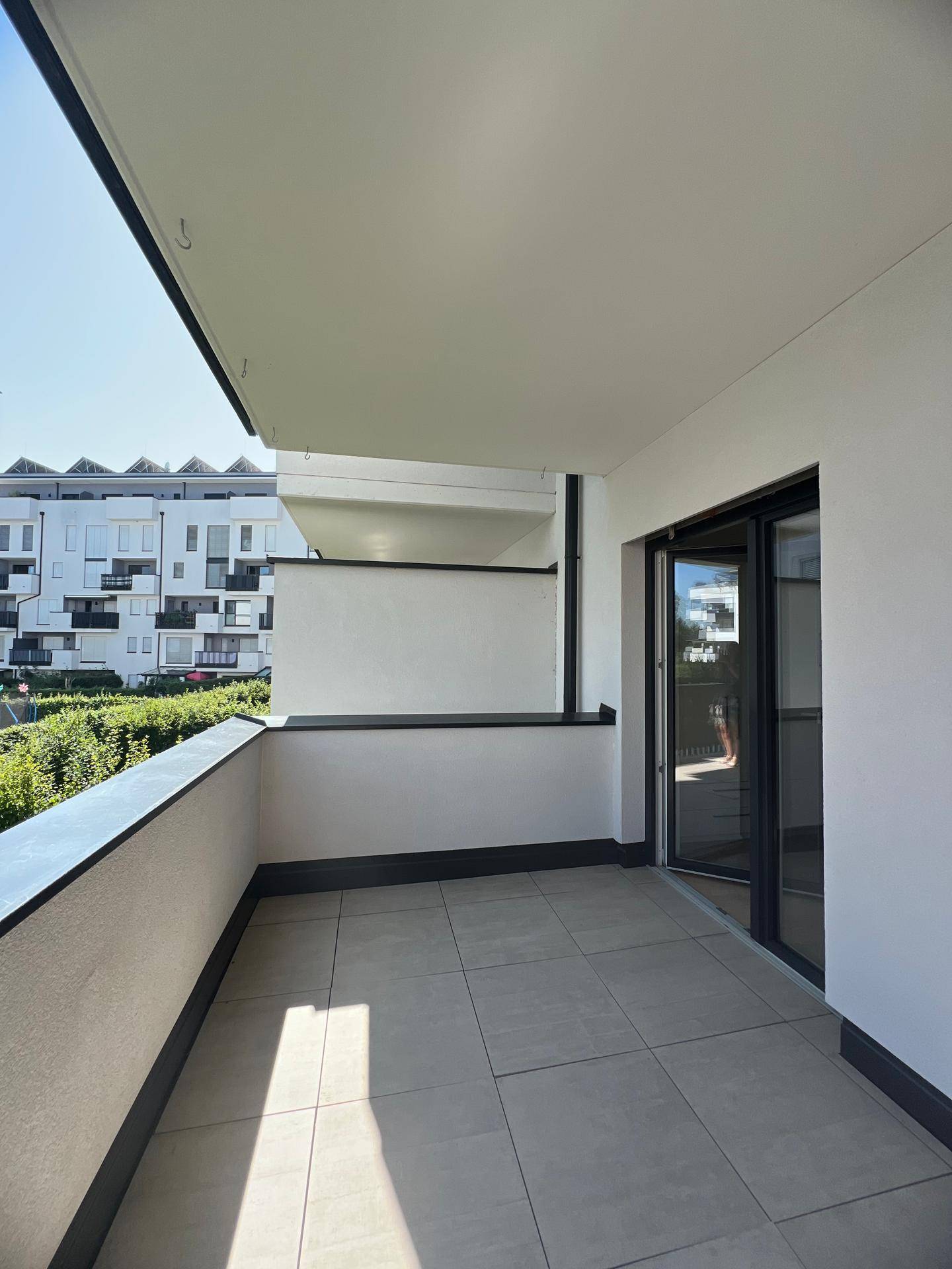 Heller Balkon mit Fliesenboden und Blick auf die umliegenden Gebäude und Grünflächen.