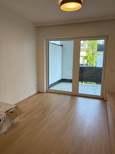 Heller Raum mit Holzboden und großem Fenster, Zugang zu einem Balkon.