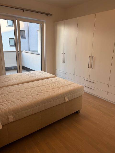 Helles Schlafzimmer mit Holzboden und weißem Einbauschrank, direkter Balkonzugang.