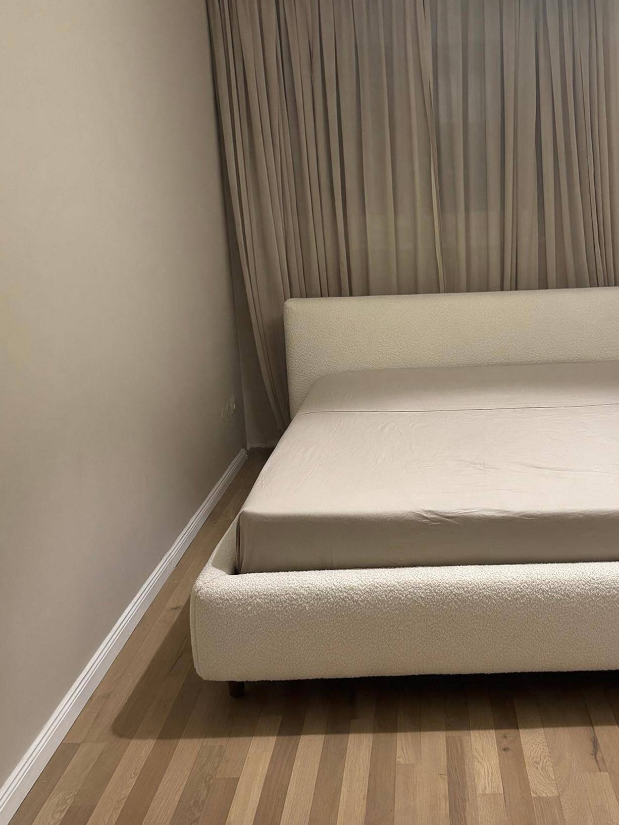 Schlafzimmer mit einem modernen, gepolsterten Bett und hellen Vorhängen, auf einem Holzboden.