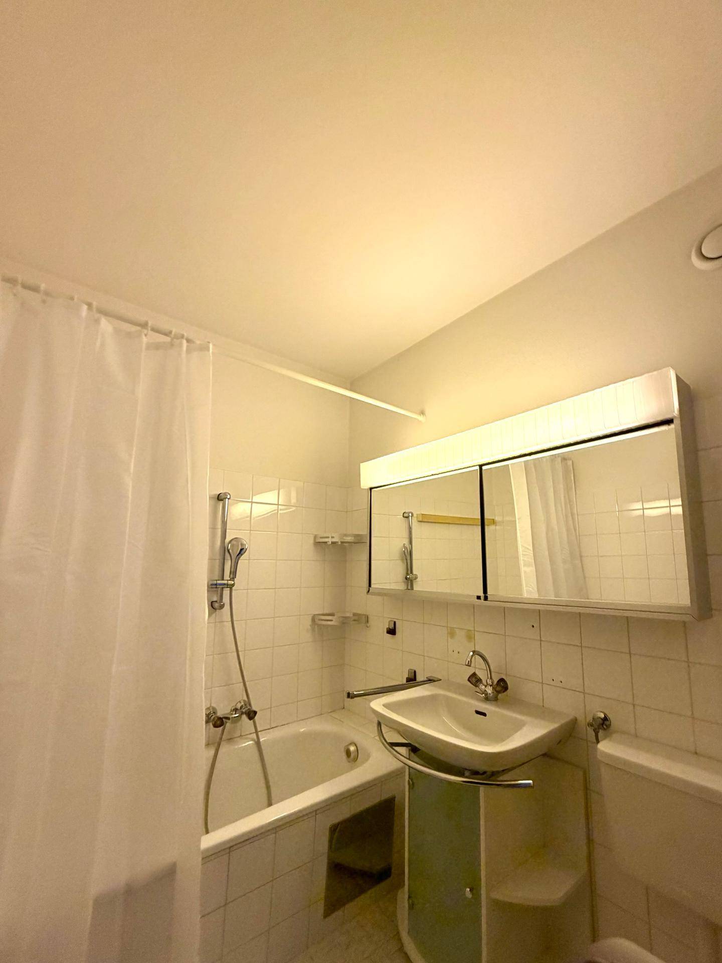 Badezimmer mit Badewanne, Duschvorhang, Waschbecken und Spiegelschrank.