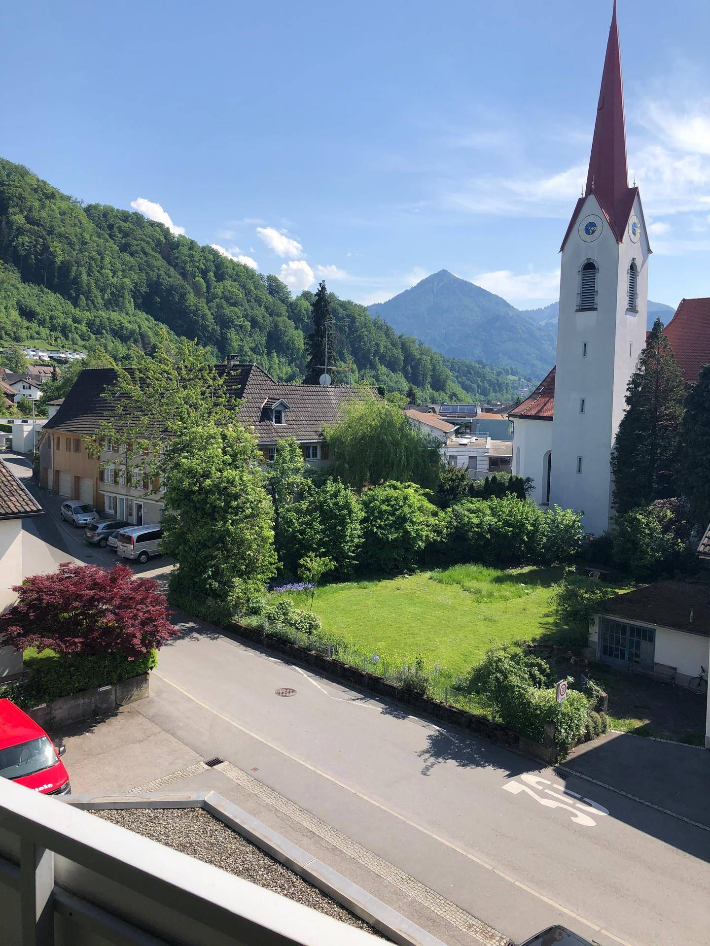 Weitläufiger Blick auf die umliegende Berglandschaft, eine Kirche und die darunterliegende Ortschaft.