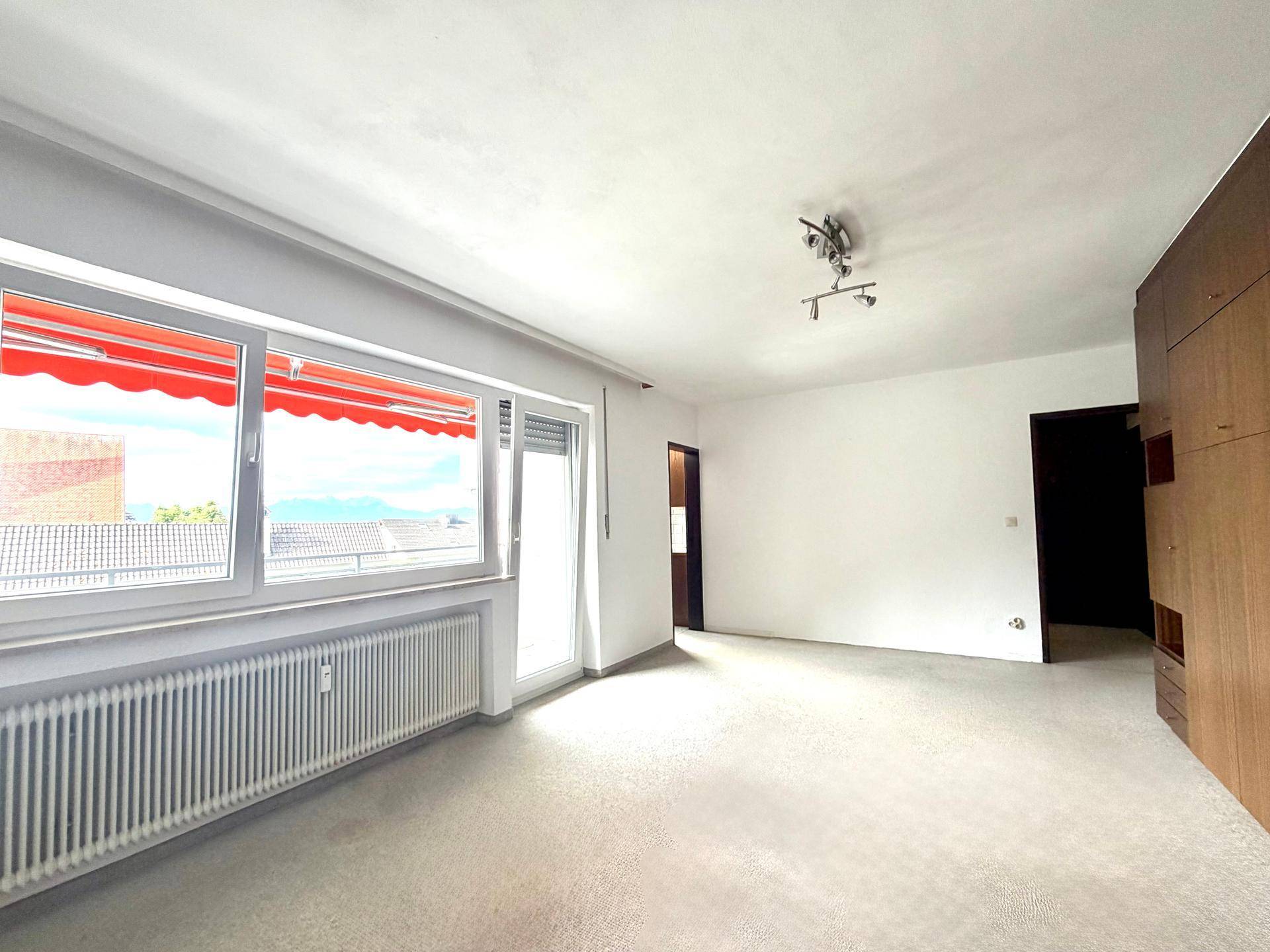 Helles Wohnzimmer mit Teppichboden, großen Fenstern und Zugang zum Balkon.