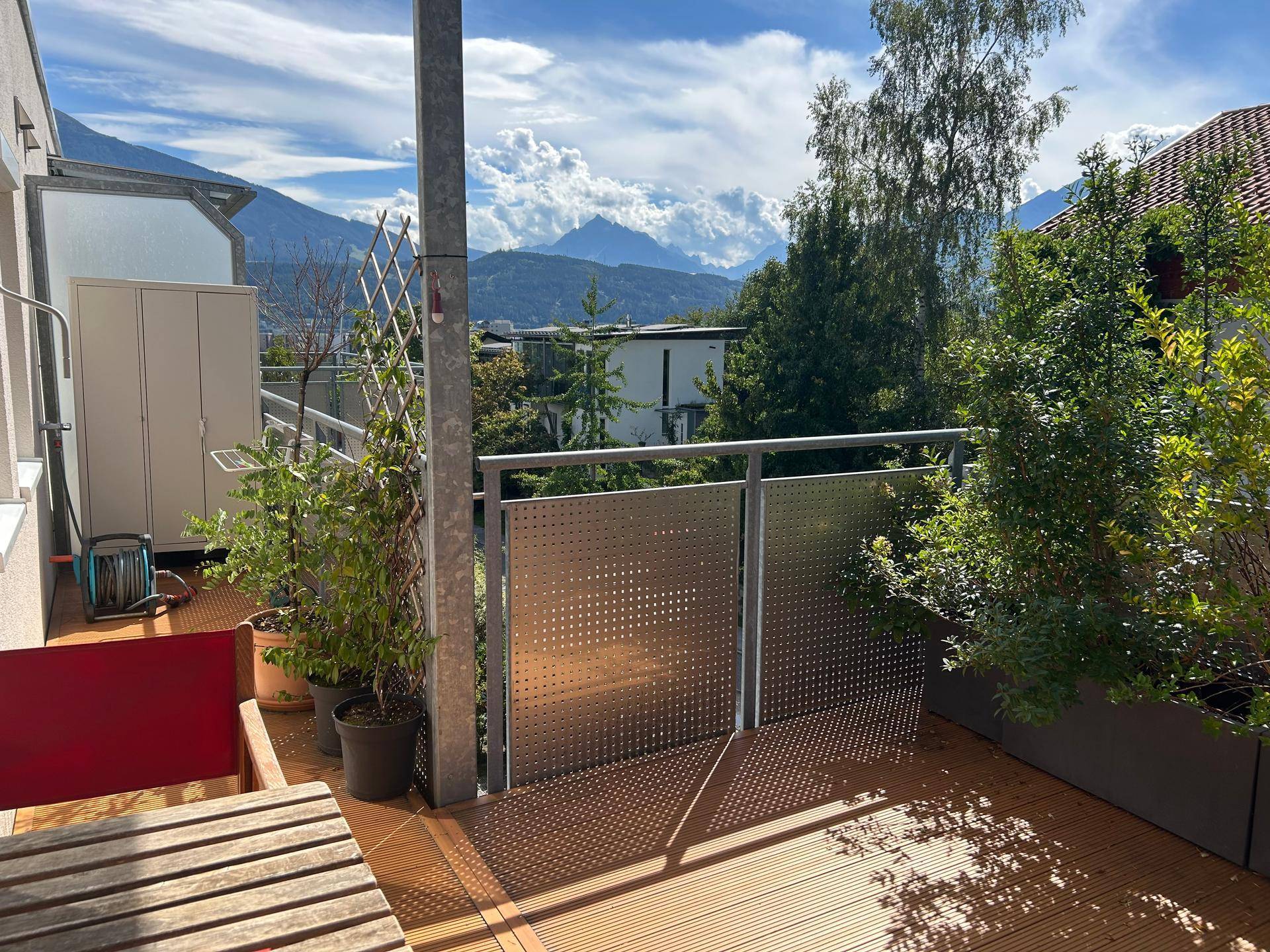 Sonniger Balkon mit Holzboden, Pflanzen und einem weiten Blick auf die umliegenden Berge.
