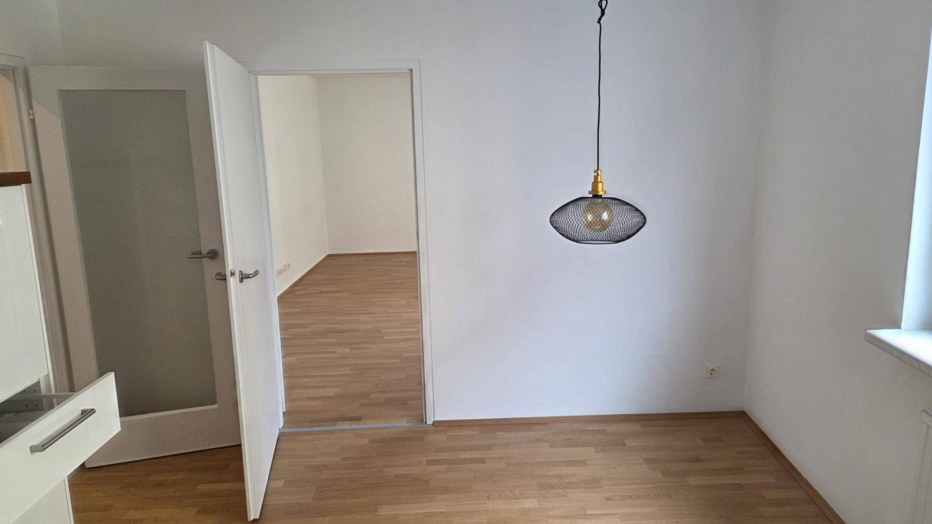 Heller Flur mit modernem Pendellicht und offenen Türen zu weiteren Zimmern mit Parkettboden.