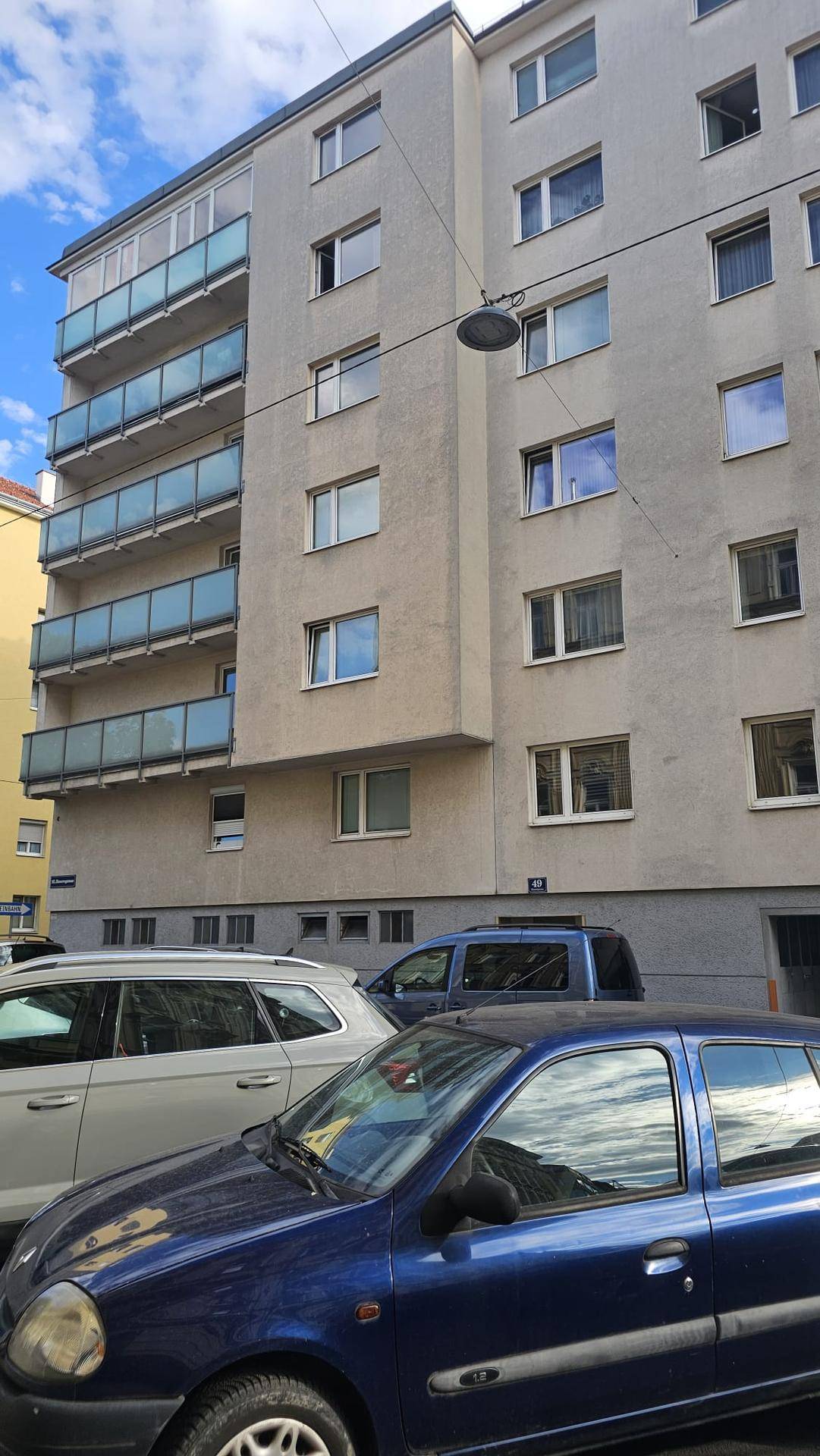 Mehrstöckiges Wohngebäude mit mehreren Balkonen und parkenden Autos davor.