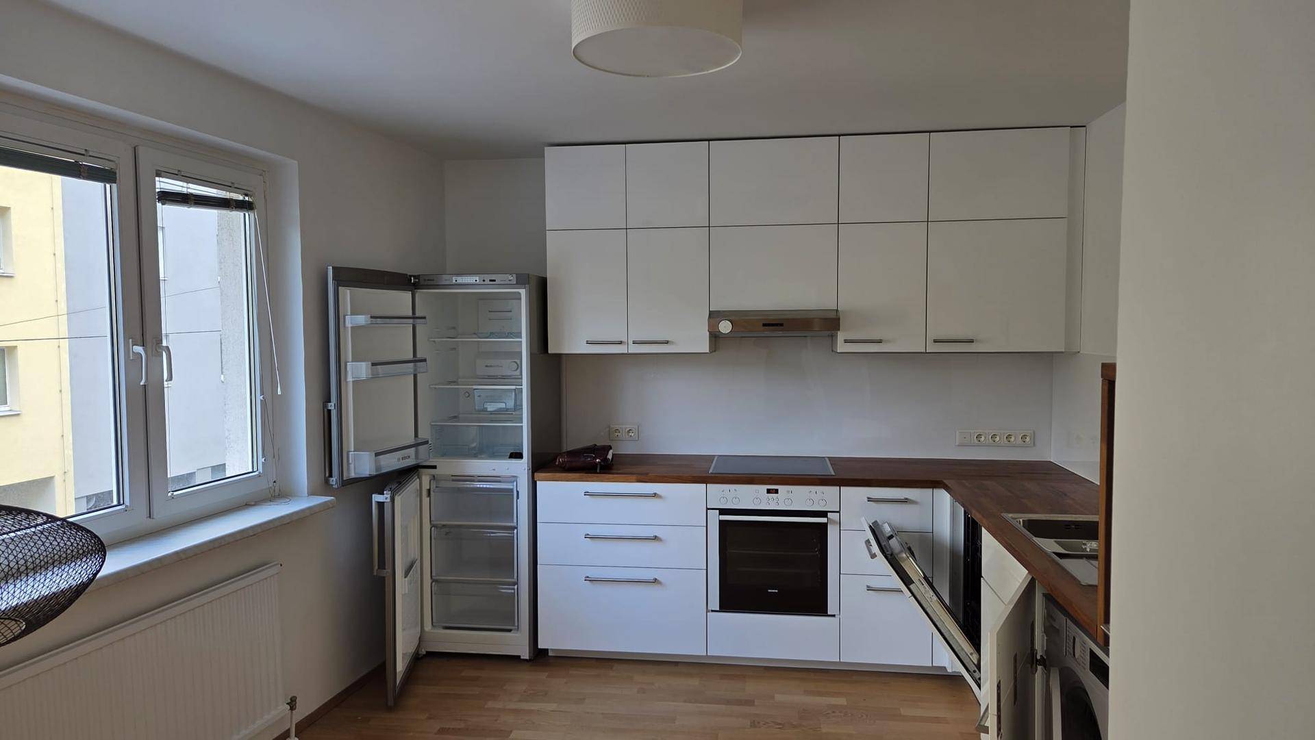 Moderne Küche mit weißen Schränken, Holzarbeitsplatten und integrierten Geräten sowie einem Fenster.