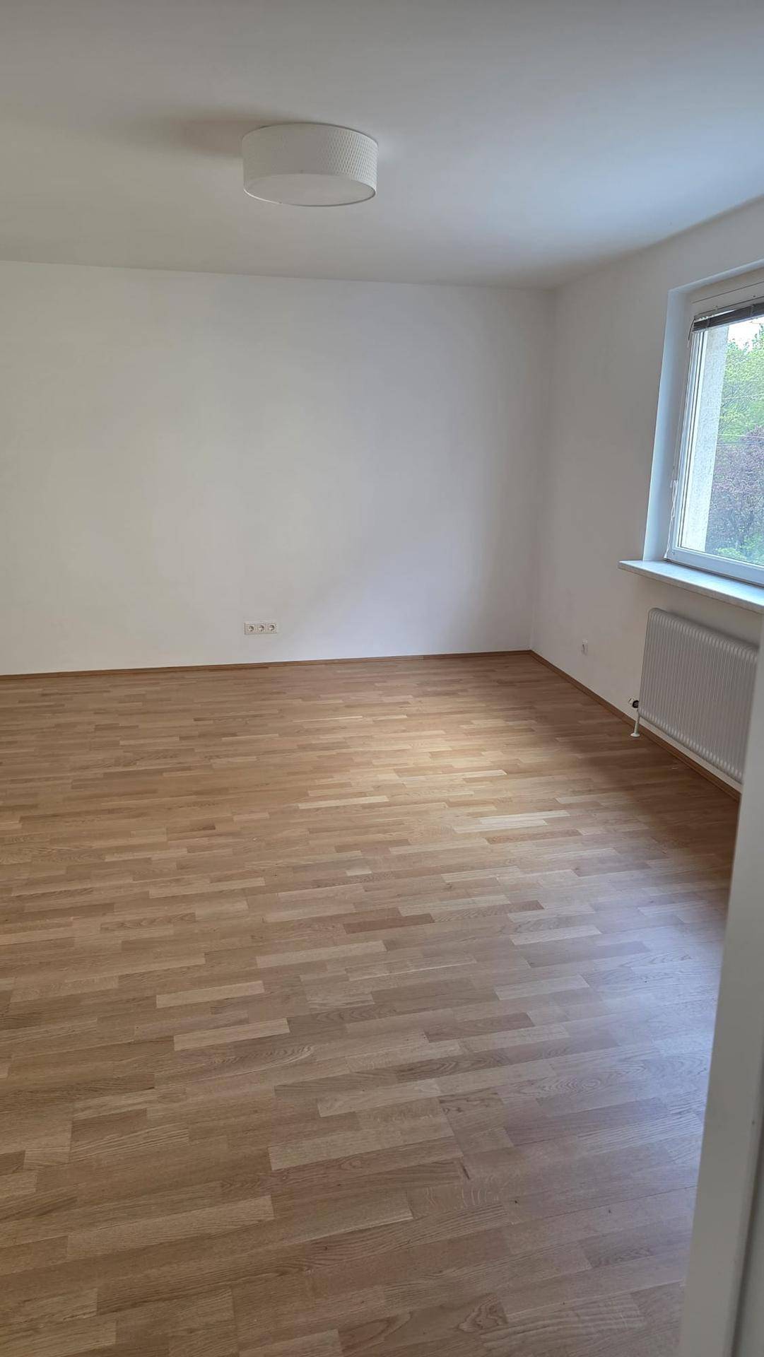 Geräumiges Zimmer mit hellem Parkettboden, weißen Wänden und einem großen Fenster für viel Tageslicht.