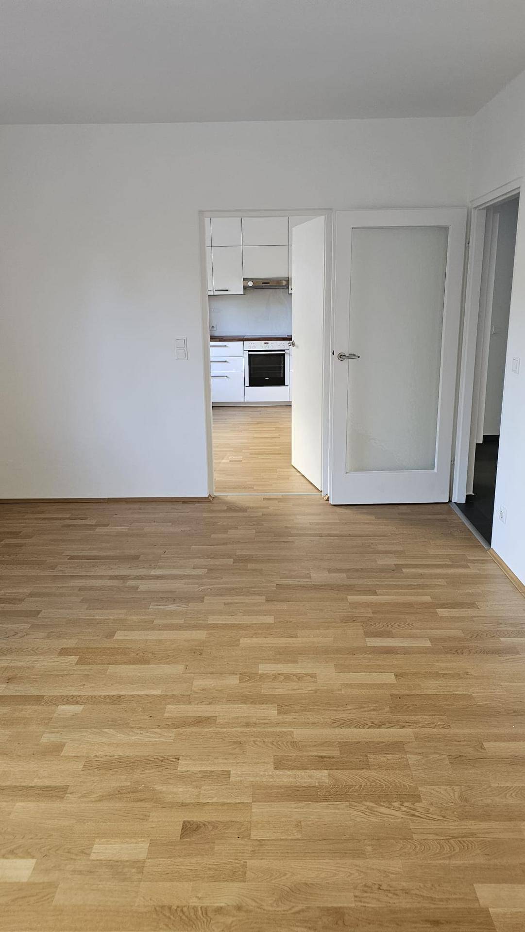 Geräumiges Zimmer mit Parkettboden und offenem Zugang zur modernen Küche.