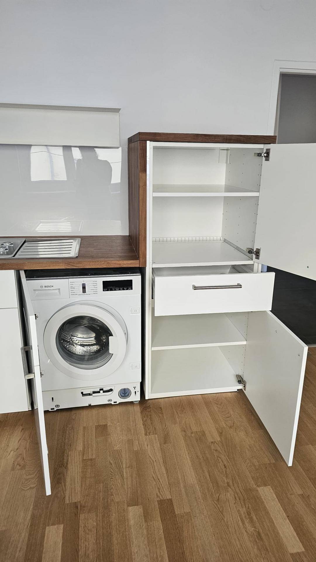 Detailansicht der Küche mit integrierter Waschmaschine und offenem Schrankfach.