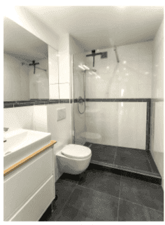Modernes Badezimmer mit weißen und schwarzen Fliesen, wandhängendem WC und begehbarer Dusche.