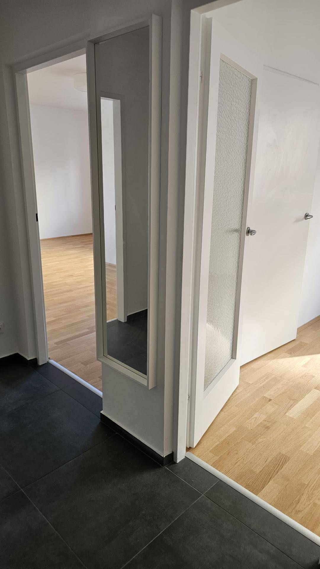 Heller Flur mit dunklen Fliesen, einem integrierten Spiegel und Zugang zu weiteren Räumen.