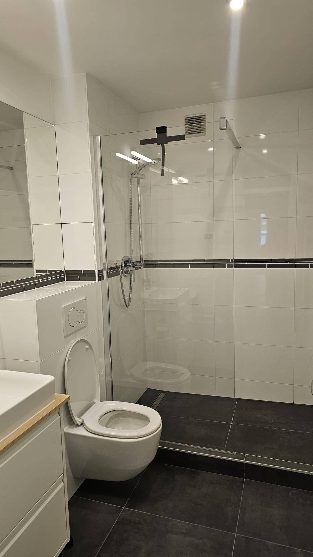 Modernes Badezimmer mit weißen und schwarzen Fliesen, wandhängendem WC und begehbarer Dusche.
