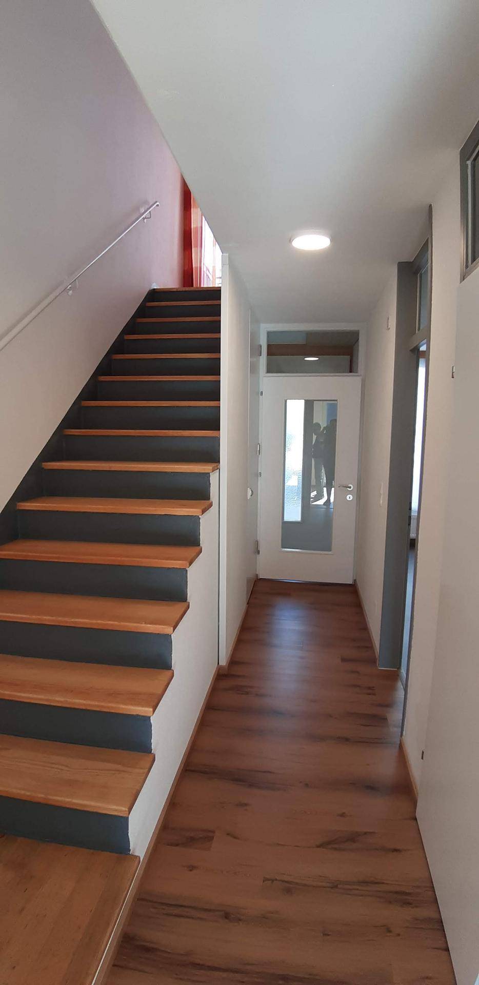 Heller Flur mit Holztreppe und Eingangstür, die zu den oberen Etagen führt.