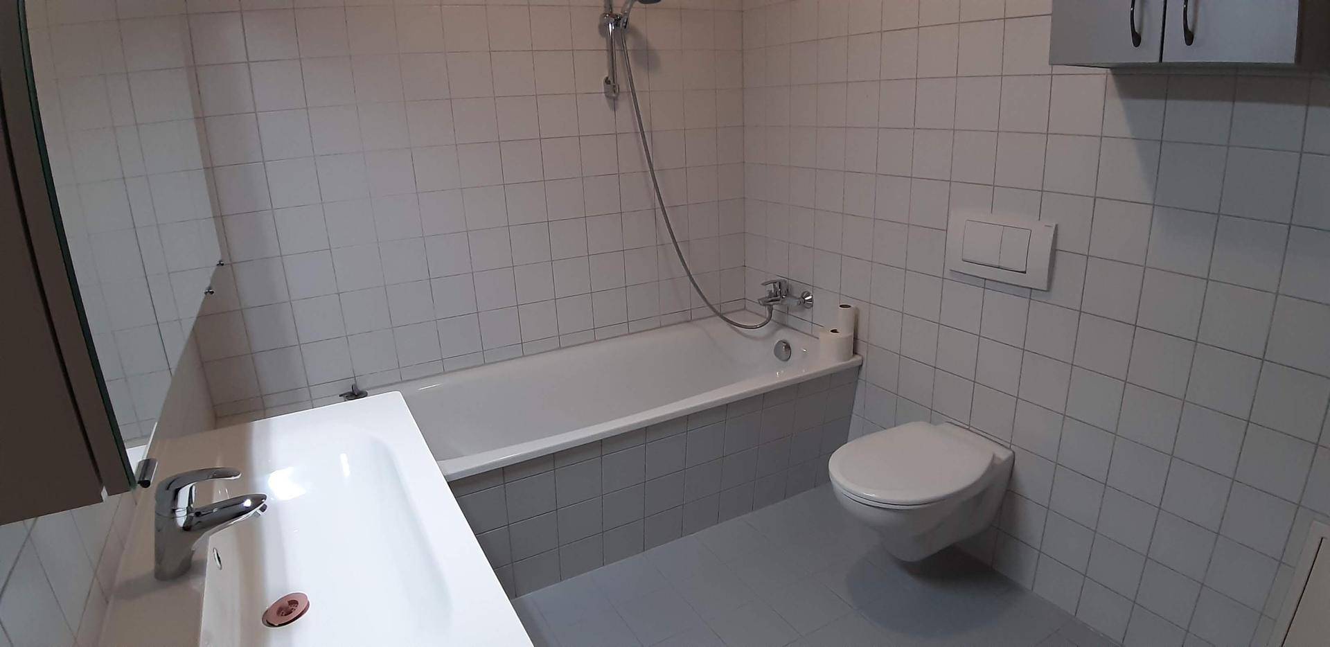 Helles Badezimmer mit Badewanne, WC und weißen Wandfliesen in gutem Zustand.