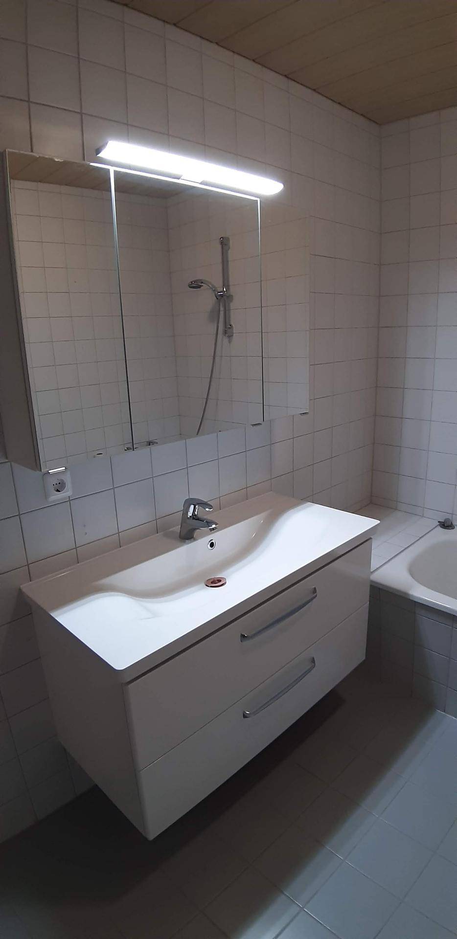 Badezimmer mit Waschtisch, Spiegelschrank und weißen Fliesen an den Wänden.