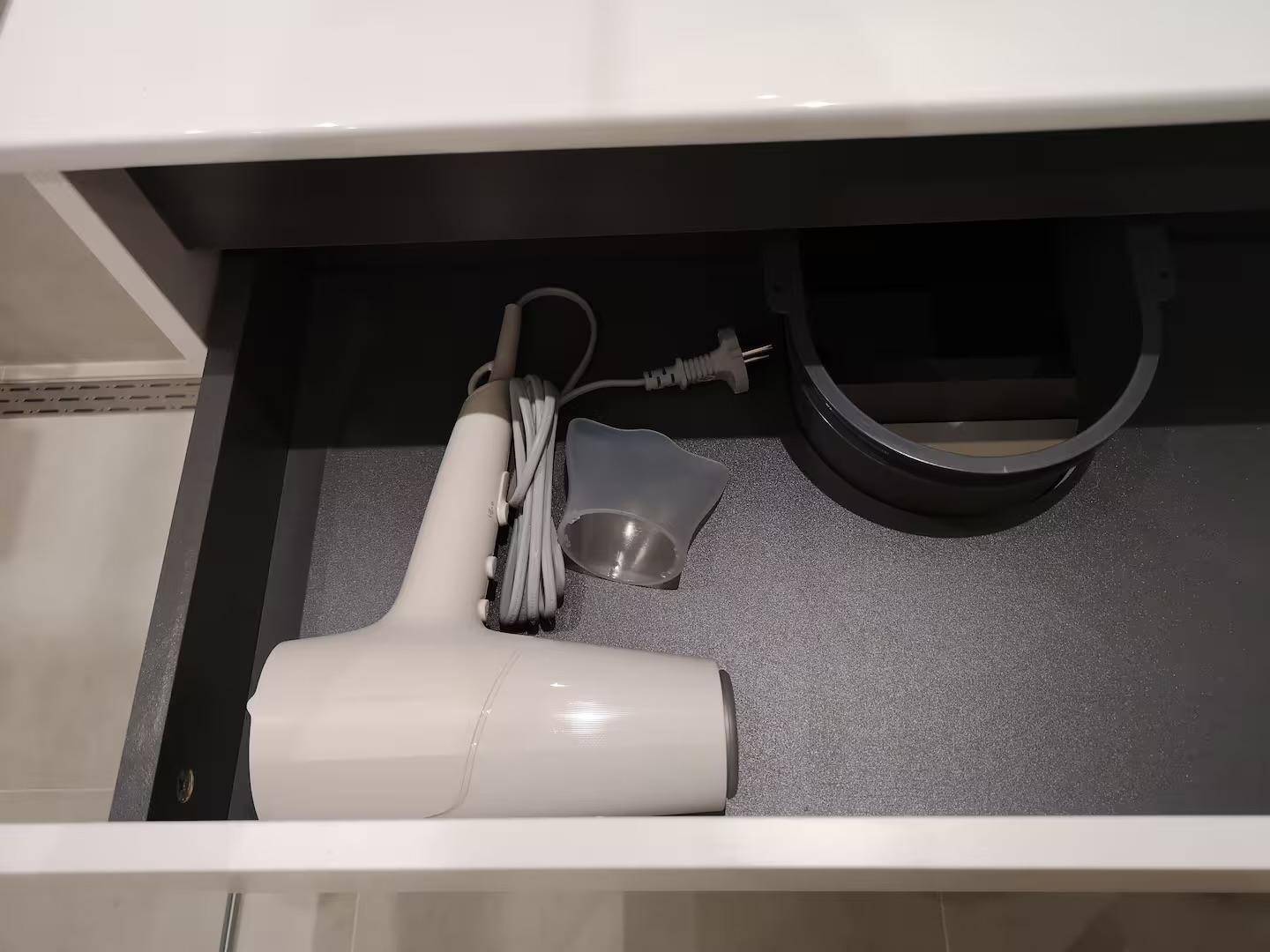 Schublade mit Haartrockner und Messbecher, ordentlich verstaut.