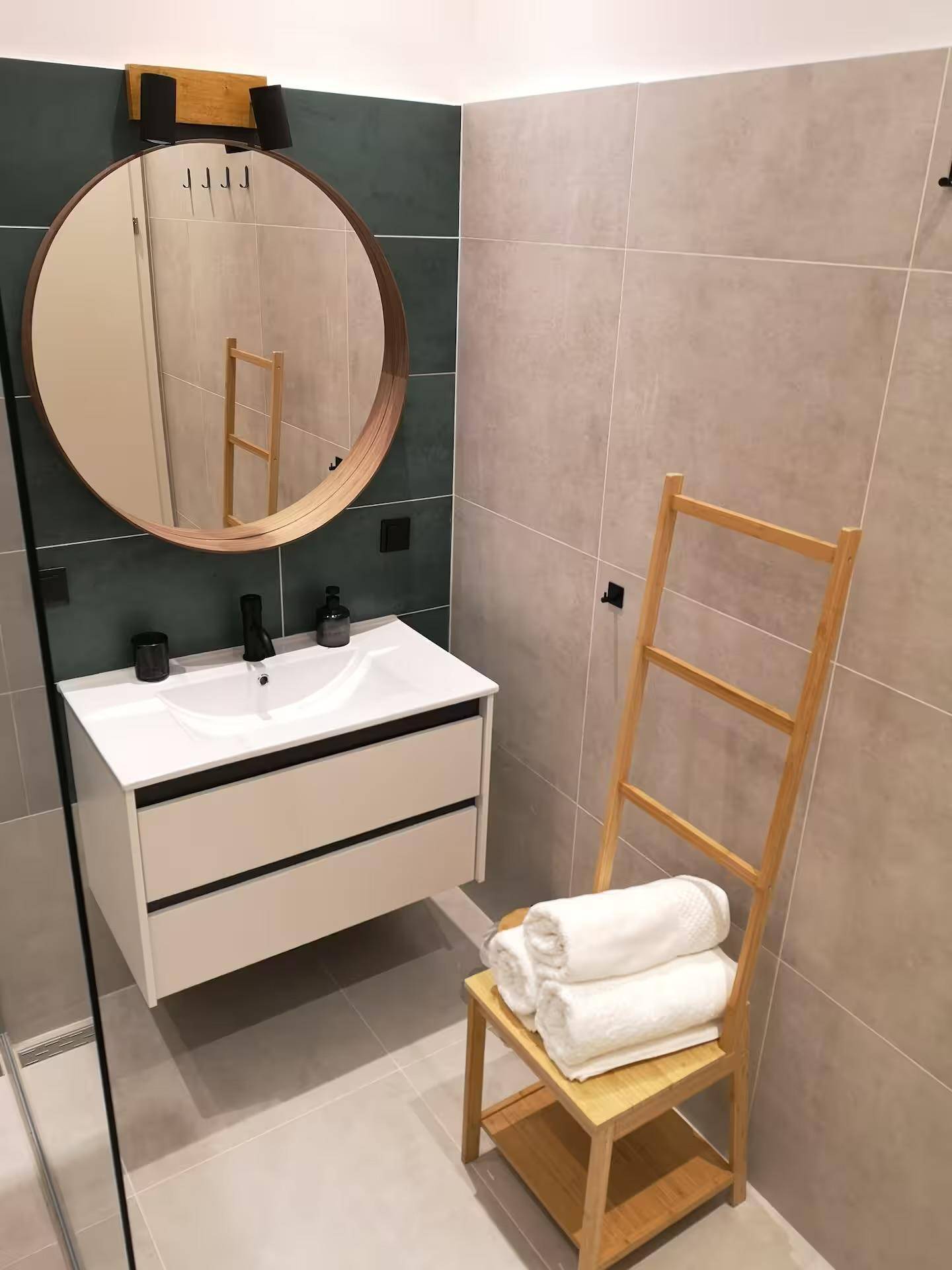 Modernes Badezimmer mit Einzelwaschbecken, rundem Spiegel und Holzhandtuchhalter.