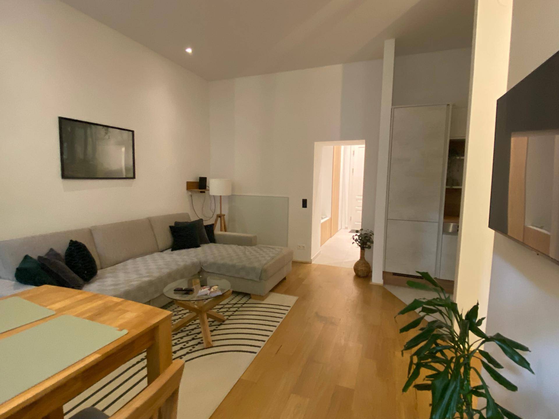 Gemütliches Wohnzimmer mit großem Ecksofa, Holzboden und Blick in den Flur.