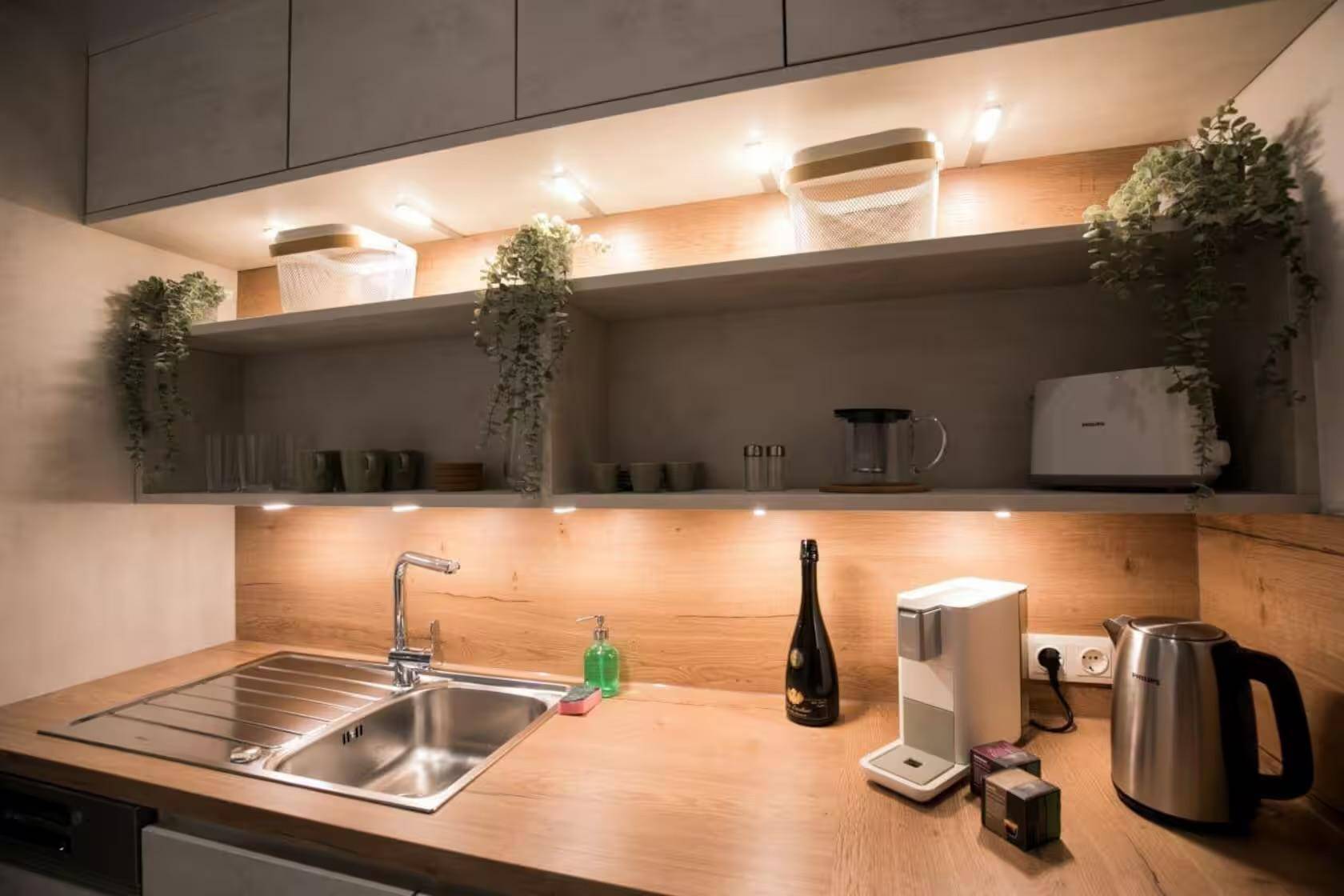 Moderne Küche mit Spüle, Küchengeräten und beleuchteten offenen Regalen.