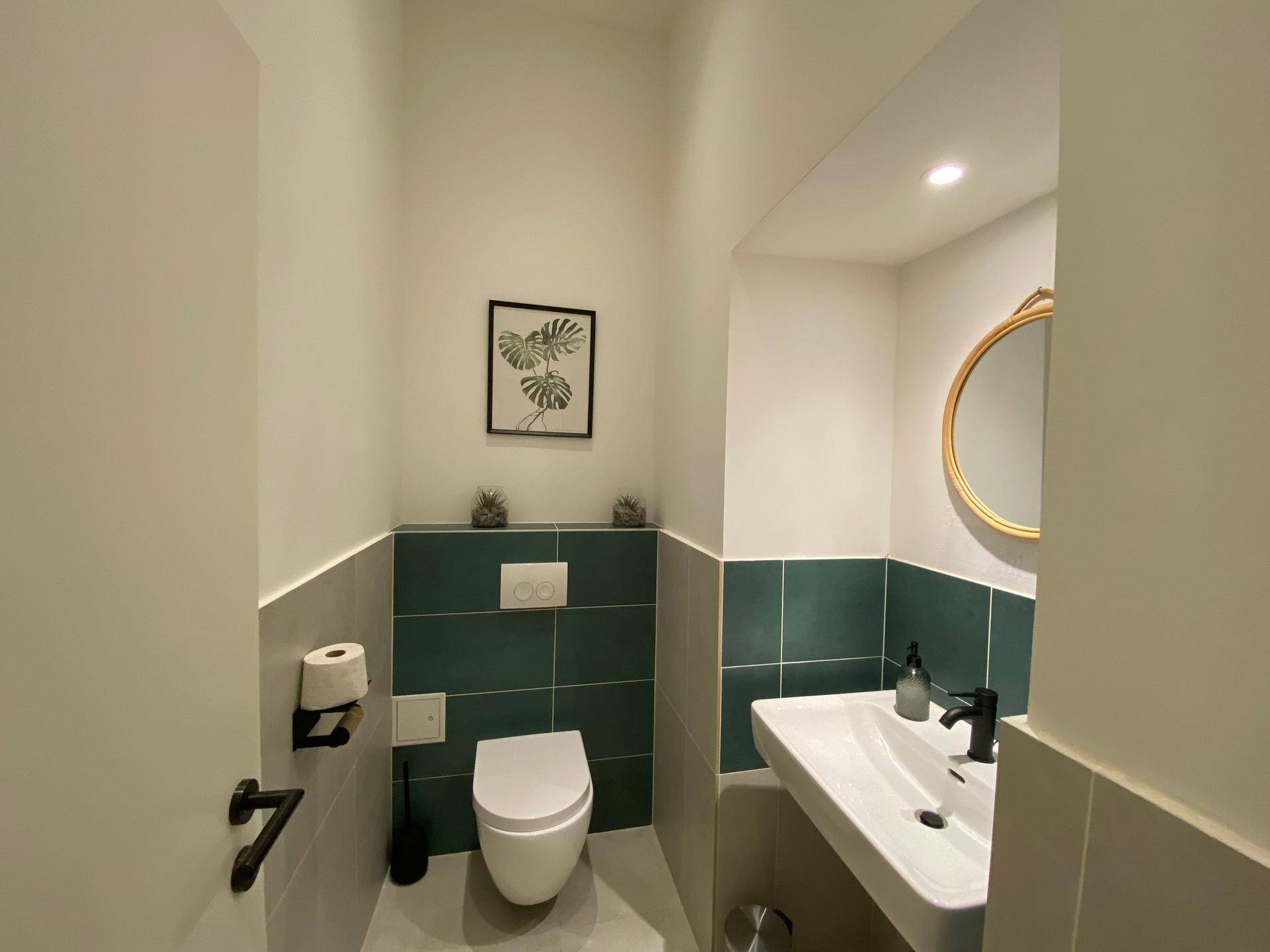 Modernes Gäste-WC mit Wand-WC, Einzelwaschbecken und stilvollen Fliesen in Grau und Dunkelgrün.