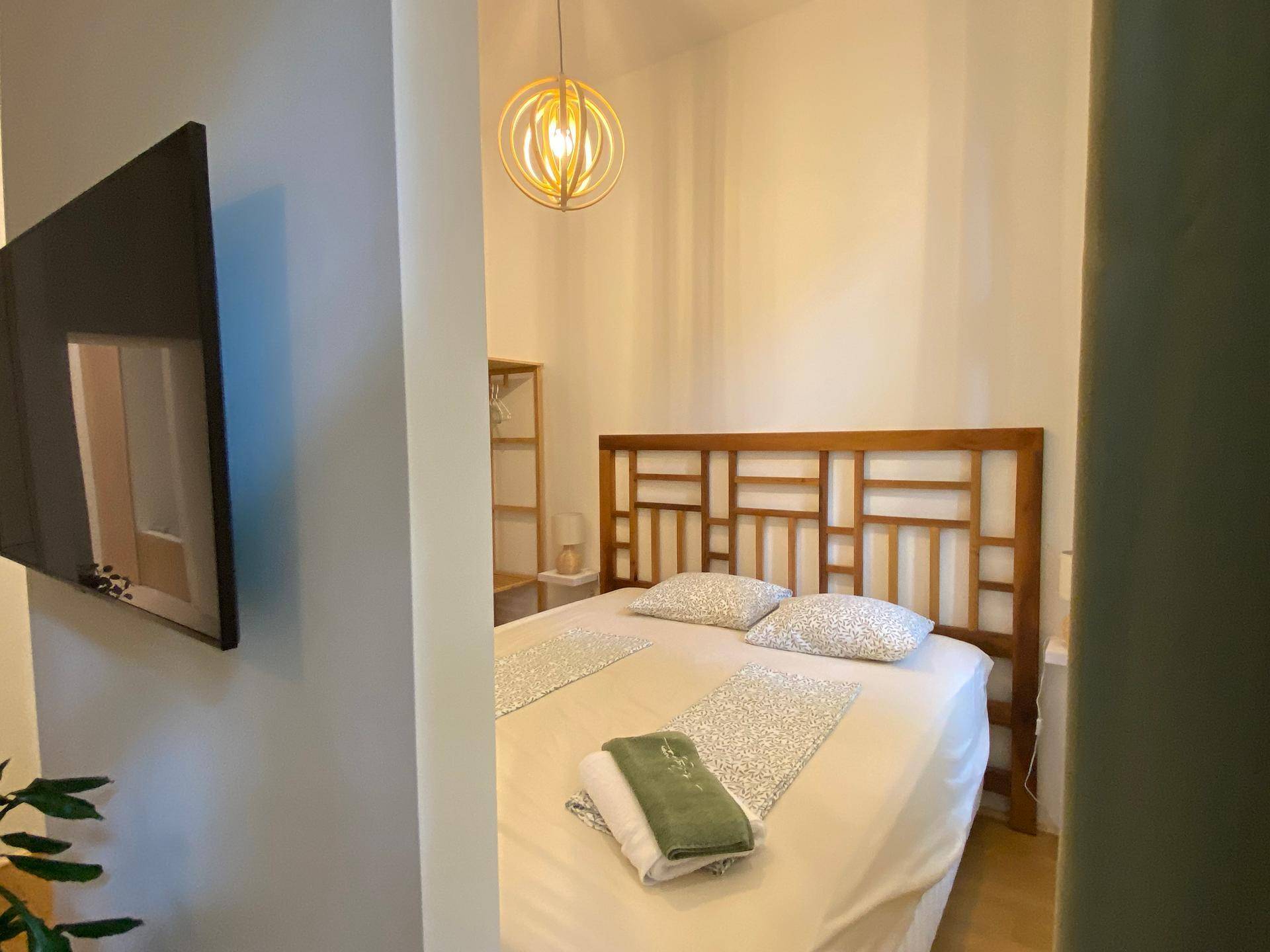 Schlafzimmer mit Holzbettrahmen, dekorativem Kopfteil und an der Wand montiertem Fernseher.