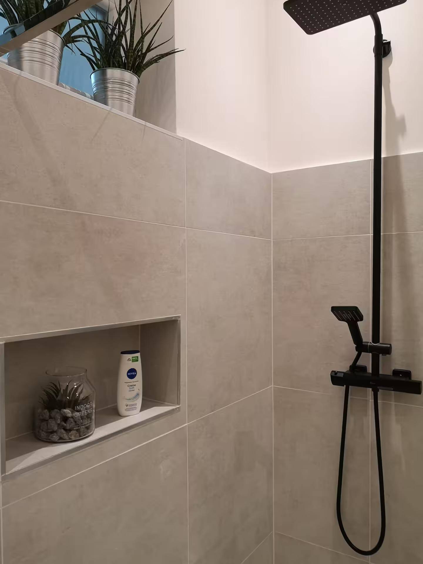 Duschbereich mit Regendusche, grauen Fliesen und praktischer Nische für Pflegeprodukte.