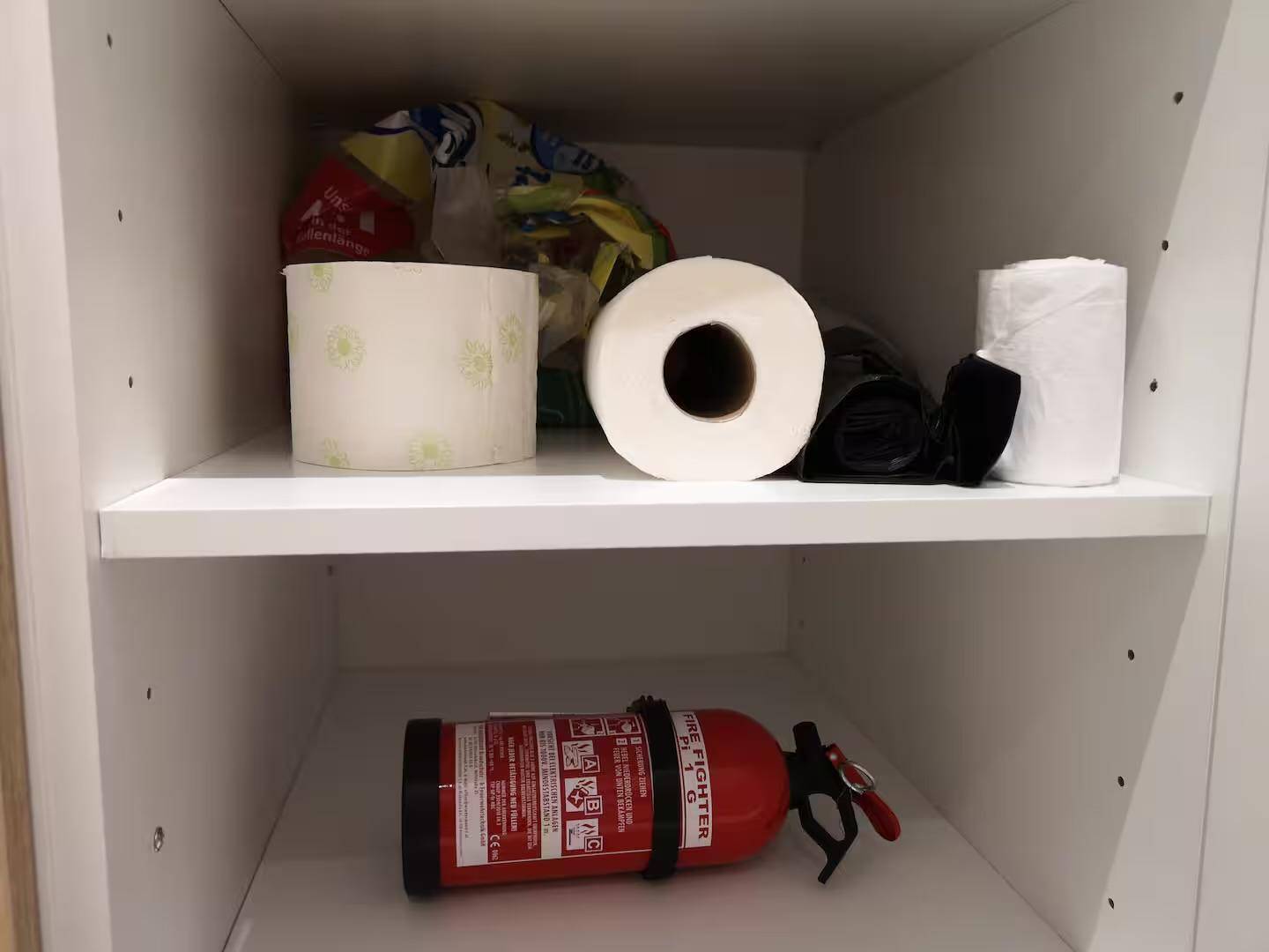Abstellschrank mit Regalen, gefüllt mit Toilettenpapier und einem Feuerlöscher.