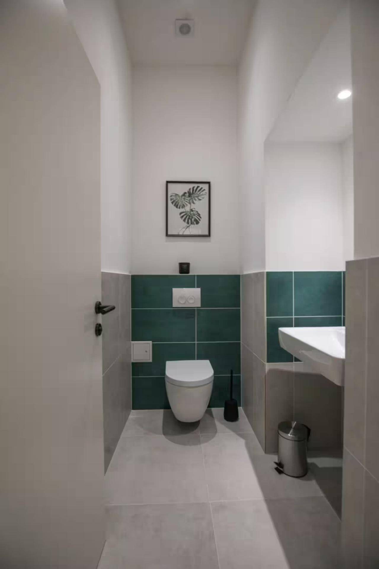 Modernes Gäste-WC mit Wand-WC, Einzelwaschbecken und stilvollen Fliesen in Grau und Dunkelgrün.